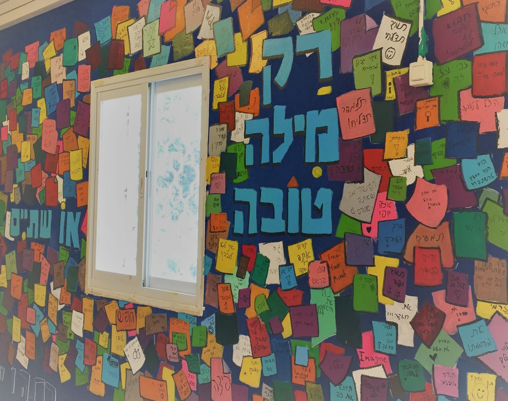 קיר צבעוני עם פתקים ומשפט 'דרך מילה טובה או שתיים' בחדר המורים